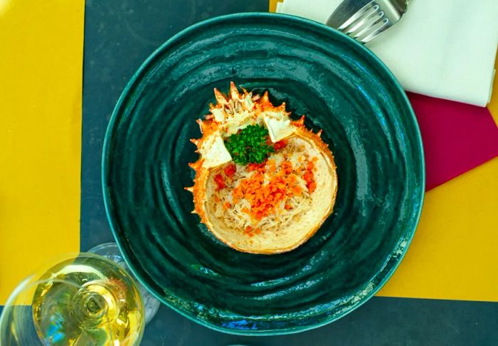 An aerial view of a dish on a dark green plate, accompanied by a glass of white wine at Corte Sconta restaurant.