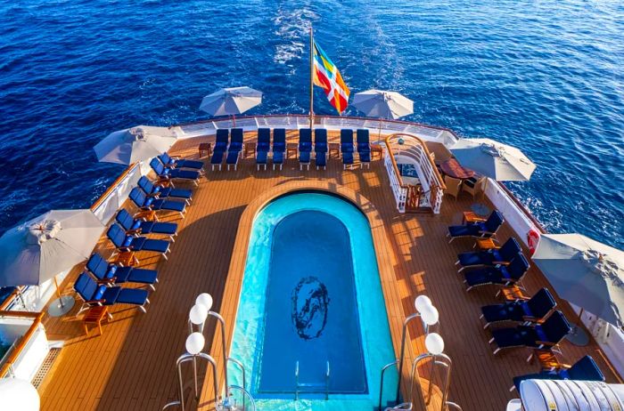 Aerial view showcasing a pool surrounded by vacant navy blue lounge chairs and a wooden deck on a SeaDream Yacht Club vessel.