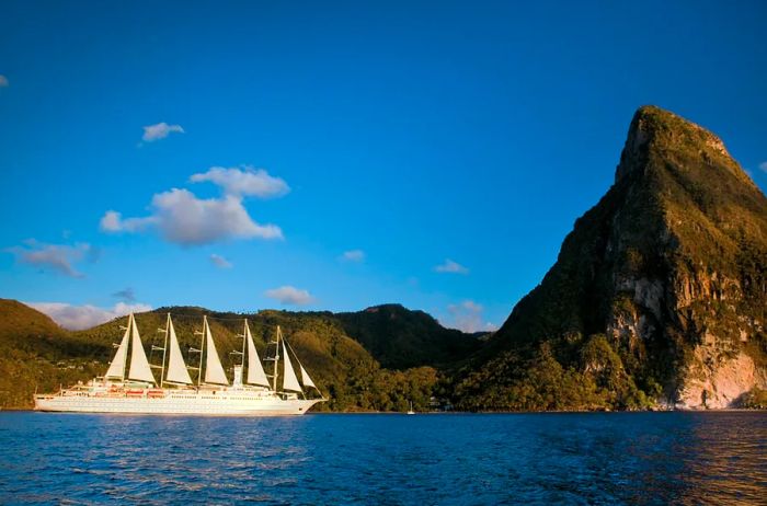 A white sailing ship from Windstar Cruises with five masts anchored next to a lush green island.