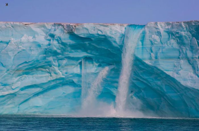 Water cascades over the edge of the turquoise-tinted Austfonna, the world’s third-largest ice cap