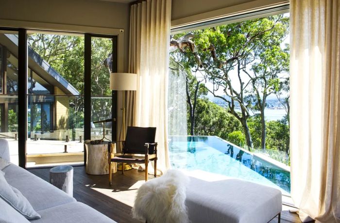 The interior of a guest room at Pretty Beach House features expansive windows that frame views of the trees and pool.