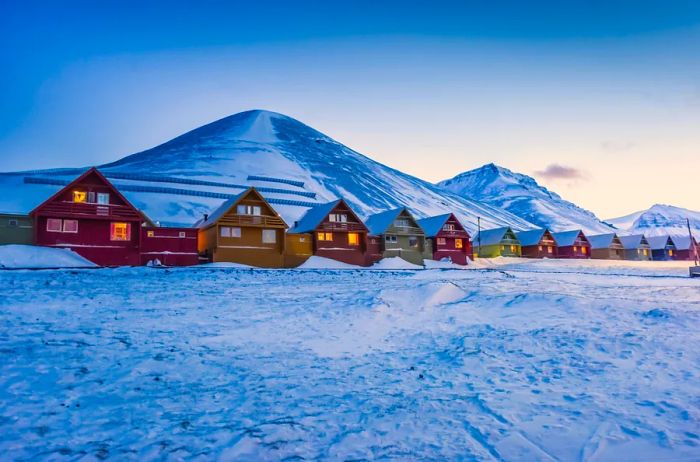 A row of vibrant houses in Svalbard, with a snowy field in front and snow-capped mountains in the background