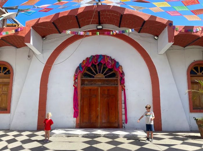 Two children playing on checkered tiles in front of a white building in the central square of Sayulita