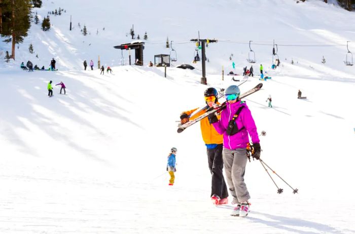 Skiers carrying their skis on their shoulders as they stroll along a ski hill