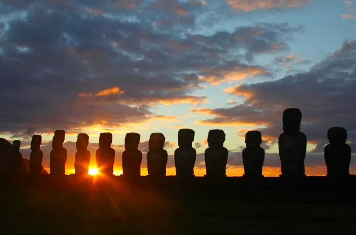 A row of statues on Easter Island silhouetted against a sunset sky.