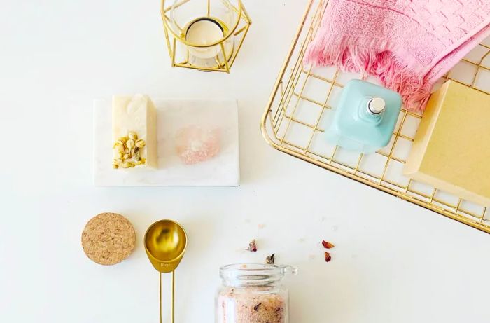 Items like a blue spray bottle, a pink towel, pink salt, and a tea candle neatly arranged at a spa.