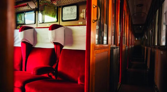 Interior view of Italy's Dante Train, featuring red seating and wooden sliding doors and panels