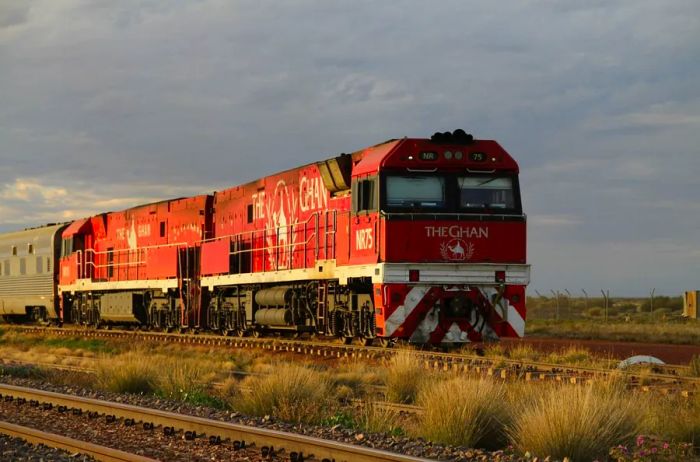 A red train traverses the tracks during a stunning sunset.