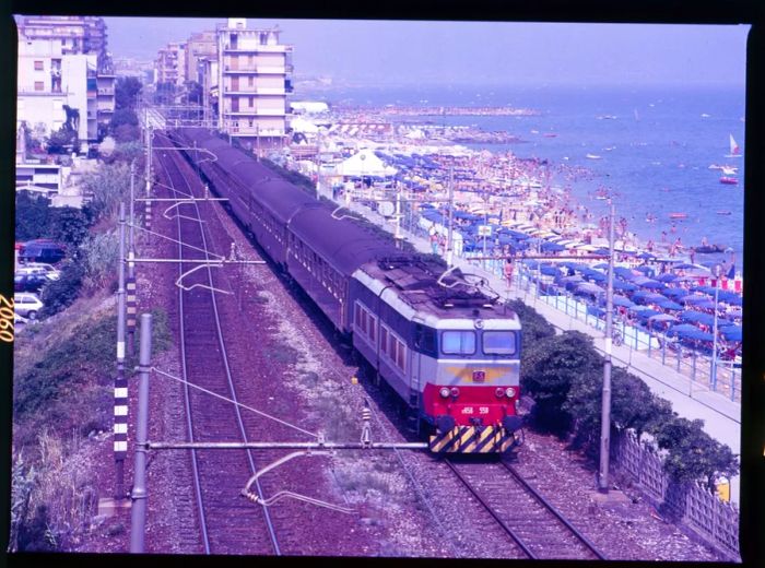 An '80s-style train in Italy, set against a backdrop of a beach dotted with umbrellas on the right