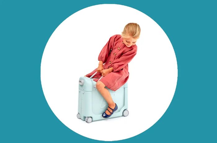 Child in a red dress riding a small blue suitcase