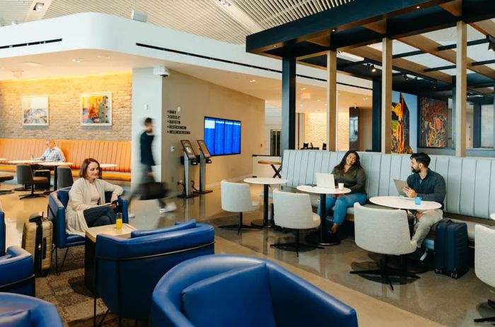 Travelers relaxing on blue armchairs and white banquettes in the United lounge at Newark airport