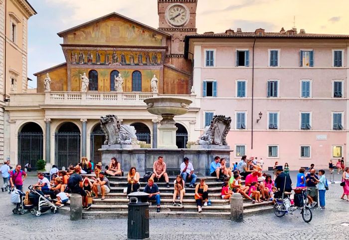 A lively scene at Piazza di Santa Maria in Trastevere, with people gathered on the steps around the fountain.