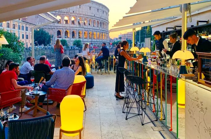 Guests seated at tables next to the outdoor Court cocktail bar, with the Colosseum as a backdrop