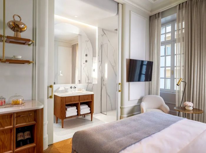 The Athenian Room at the Dolli in Athens features expansive windows dressed with floor-to-ceiling curtains and a luxurious marble bathroom.