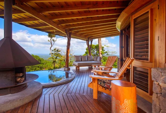 The lodge's porch features a fireplace, small pool, wooden chairs, and a sofa with views of the jungle.