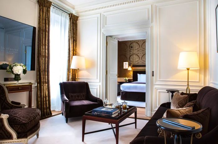 This luxurious suite at La Réserve Paris features elegant wingback chairs, pristine white carpets, and grand floor-to-ceiling drapes.