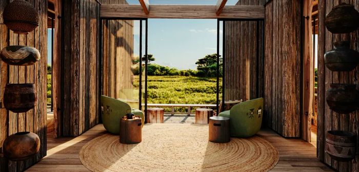 A room with wooden walls and floors, featuring two chairs and side tables that face an open view of a grassy field and trees.