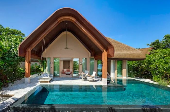 A biophilic lodge featuring a triangular roof and patio, with a pool in the foreground.
