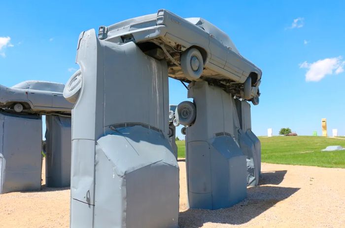 Gray Carhenge, featuring cars positioned vertically in the ground with one balancing horizontally on top.