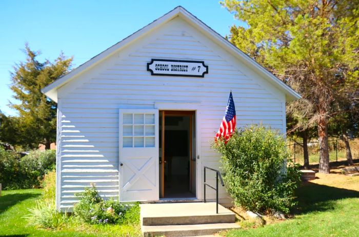 The iconic one-room schoolhouse at Mansion on the Hill, complete with an open door and a U.S. flag standing proudly beside it.