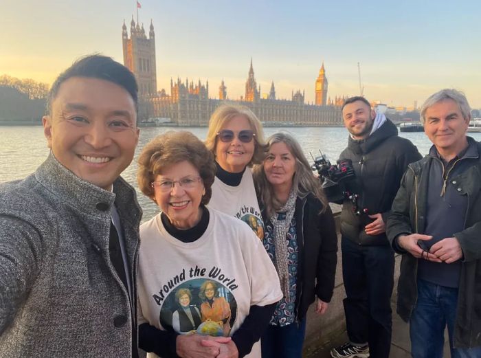 Ellie Hamby and Sandy Hazelip in London, surrounded by fans, with the Thames River and Houses of Parliament in the background.