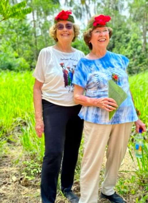 Ellie Hamby and Sandy Hazelip outdoors, proudly wearing their red flower hats.