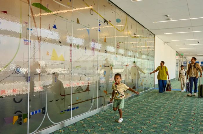 A child joyfully runs along a segment of the iconic PDX carpet, celebrated for its retro 1980s pattern, while nearby stands a vibrant installation by local artist Yoonhee Choi.