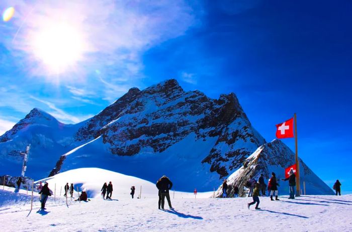 About 10 individuals standing on a snowy mountainside with the Swiss flag to the right