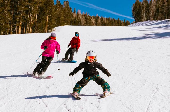 Three children gliding down a snow-blanketed slope on skis and snowboards.