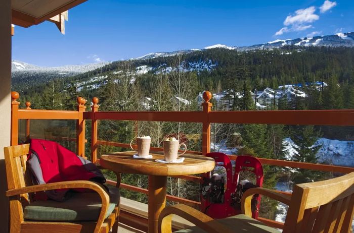 Two wooden chairs and a small table on a deck, set against a backdrop of snow-capped mountains in Whistler.