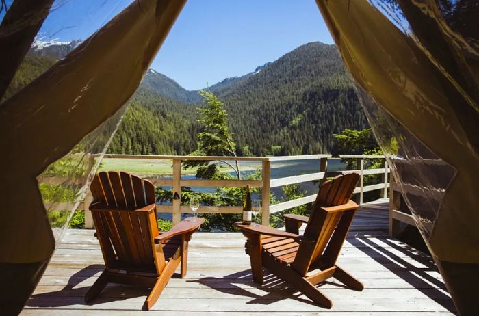 A view of lush forested hills from the deck of a Clayoquot suite, featuring two Adirondack chairs.