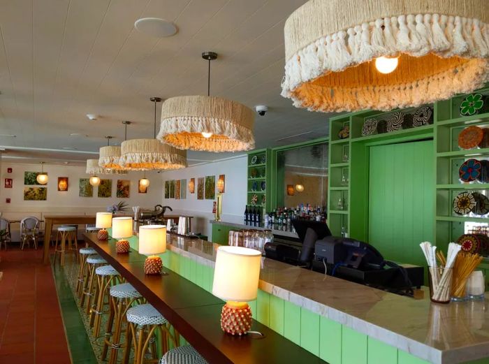 A vibrant bar with green walls and fringed pendant lighting enhances the atmosphere at the Sofitel Legend hotel.