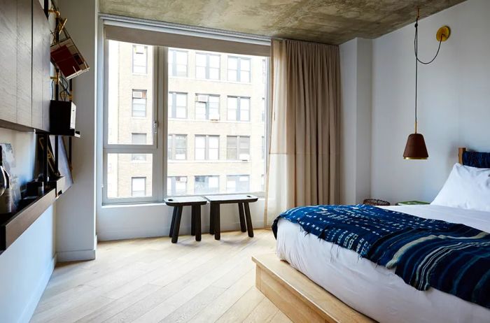 Interior of a guest room at the Made Hotel, showcasing bronze shelves and intricately hand-carved benches next to a large window.