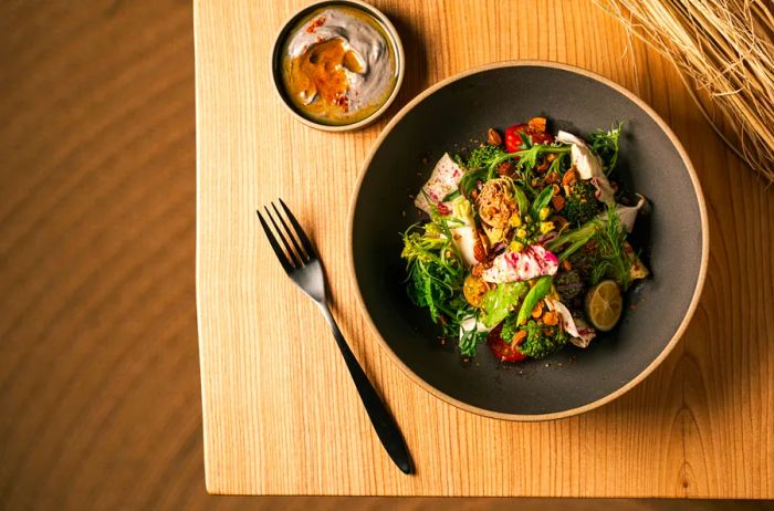 Aerial view of a bowl filled with assorted vegetables placed on a light wood table, accompanied by a fork