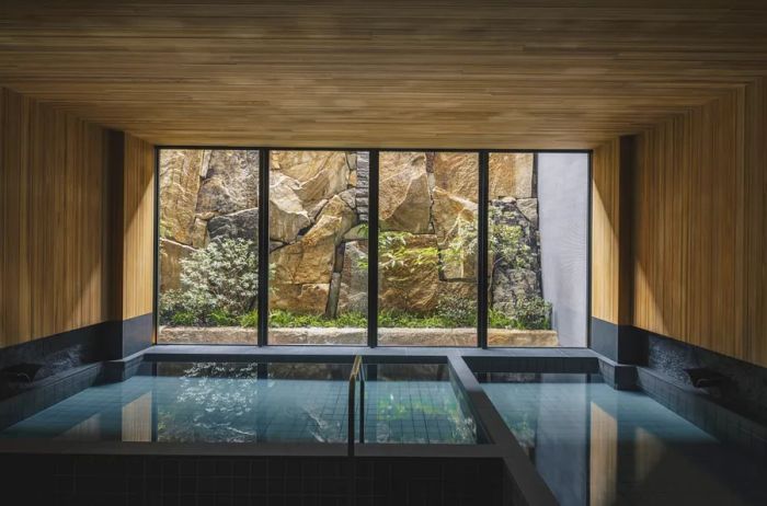 Wood-paneled spa bathhouse area at Six Senses Kyoto, featuring floor-to-ceiling windows with views of a rock-walled garden