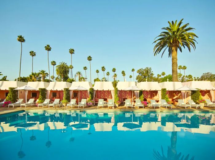 At the Beverly Hills Hotel, pink cabanas line the poolside, framed by towering palm trees in the background.