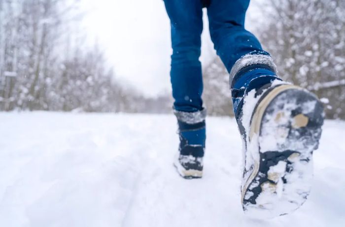 A close-up of a person walking through snow, showcasing their legs and feet