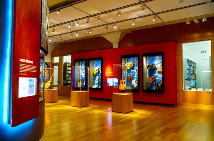 Inside the Woody Guthrie Center, showcasing an exhibit adorned with vibrant red walls and guitars displayed behind glass cases.