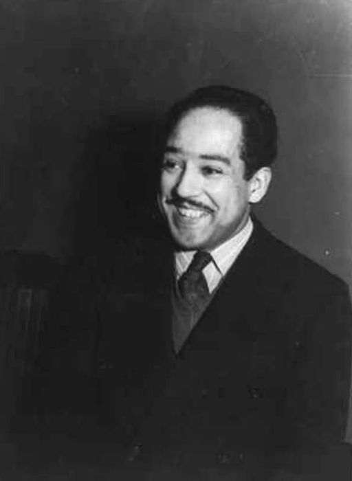 A black and white image capturing Langston Hughes with a warm smile.