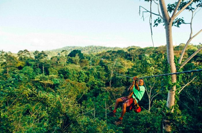 Man in a green shirt ziplining through a forest