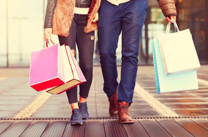 Two individuals holding hands with multiple shopping bags, captured from the waist down.