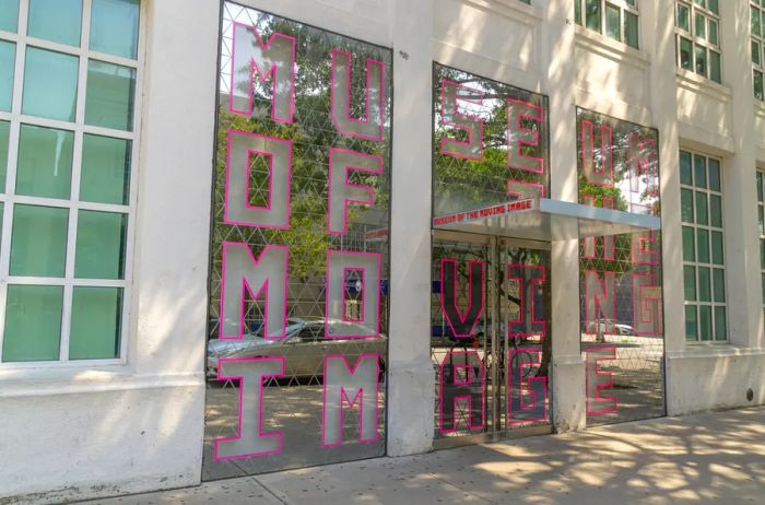 The entrance of the Museum of the Moving Image features large windows, showcasing its sleek white modern architecture in the Astoria neighborhood of Queens, New York City.