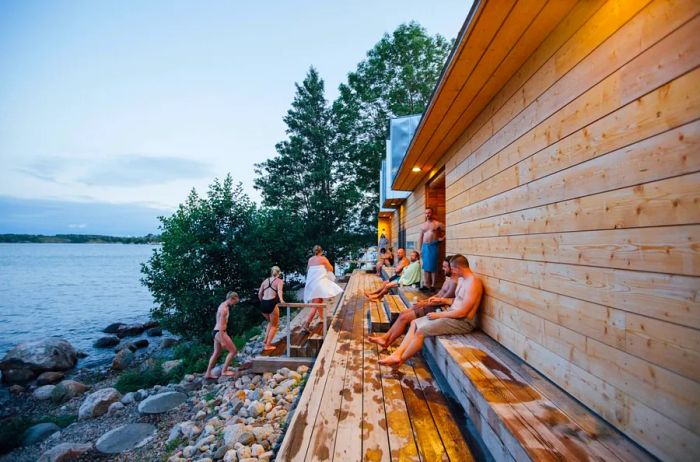 People cooling off outside a Finnish sauna in Helsinki, situated by a serene lake.