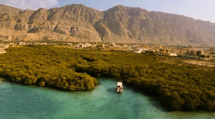 A boat glides through the waters of Suwaidi Pearl Farm, situated in the fishing village of Al Rams, against a backdrop of mountains.