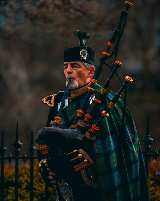 An outdoor bagpipe player dressed in blue and green tartan in Scotland, United Kingdom.