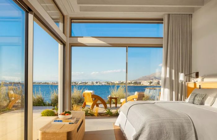 A corner bedroom adorned with modern blonde wood furnishings and stunning coastal views from floor-to-ceiling windows.