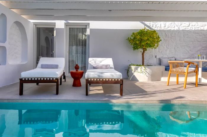 Two lounge chairs beside a sparkling blue pool at Patmos Aktis, a Luxury Collection Hotel in Greece