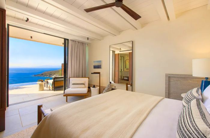 This double room at Odera Tinos offers a stunning sea view, featuring white walls, ceilings, and floors, along with a spacious bed adorned with a white comforter.