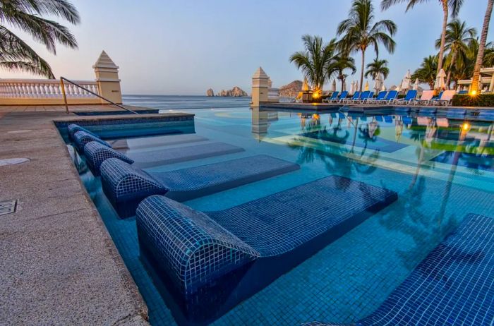 A swimming pool at a resort featuring empty lounge chairs partially submerged in the water