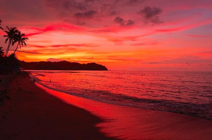 A picturesque sunset over a beach, with two people strolling along the shoreline in the background.